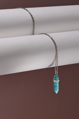 Close-up shot of a steely chainlet with a pendant in the form of screw with a fitted-in green-blue gemstone similar to a turquoise. The glazy gemstone is elongated and conical.  © RedUmbrella&Donkey