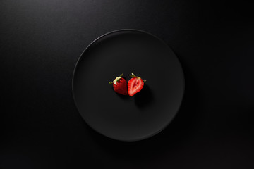 One sliced strawberry served in black plate on moody black background. Top view. Healthy diet...