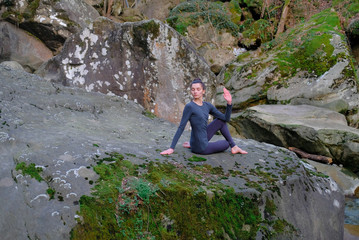 Young slim woman practicing yoga outdoors on big moss rock. Unity with nature concept. Girl in seated spinal twist pose