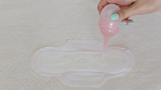 A girl pours water on a menstrual sanitary pad. Leakage protection concept, close-up