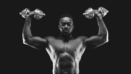 Fototapeta na wymiar African american bodybuilder pushing barbells up, working out