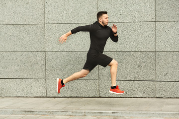 Young man jogging in city against grey urban wall, copy space, side view