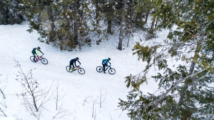 Aerial view of mountain bikers riding on road in forest outdoors in winter.