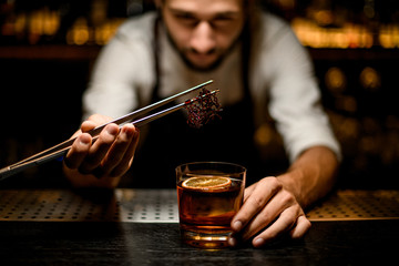 Professional bartender adding chilled brown caramel with twezzers to the cocktail with ice cubes