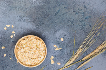 Oat flakes in wooden utensil, plant on blue concrete background. Cooking, recipe concept. Top view, flat lay, copy space