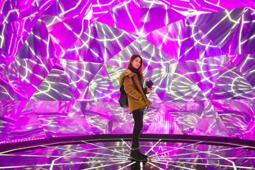 Young asian woman traveler posing on the stage with neon colored lights in background.