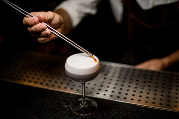 Bartender decorated scum of the delicious light violet color cocktail with a yellow flower petals