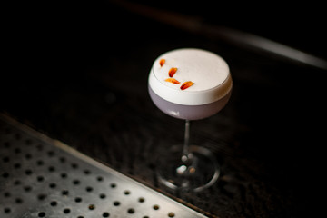 View from above glass with a delicious light violet color cocktail with a white scum decorated with yellow flower petals