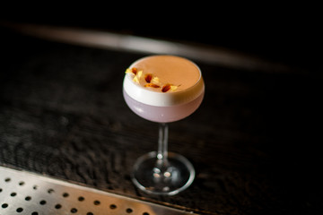 View from above glass with a delicious violet color cocktail with a white scum decorated with yellow flower petals