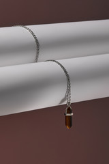 Close-up shot of a steely chainlet with a pendant in the form of screw with a fitted-in brown gemstone similar to a cat's-eye. The glazy gemstone is elongated and conical.  © RedUmbrella&Donkey