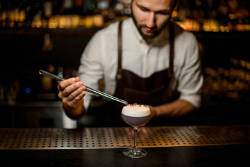 Professional bartender decorated scum of the delicious light violet color cocktail with a yellow and purple flower petals