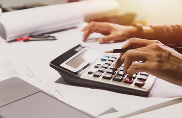Concept architects, Hand of asian young man engineering use calculator for calculation number of structural materials writing On the desk with a blueprint in the office.