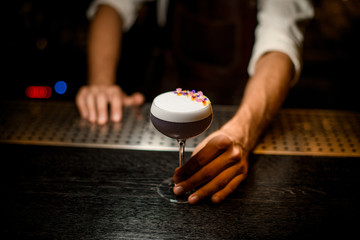 Bartender serving a cocktail with white scum decorated with flower petals on the bar counter