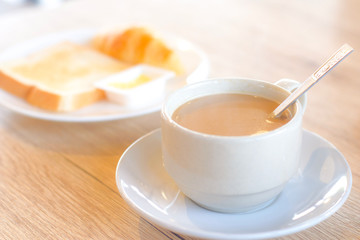 Fresh delicious breakfast with hot coffee in white cup and blur crispy toasts on wooden table.
