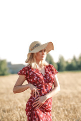 YOUNG AND BEAUTIFUL GIRL IN THE DRESS AND HAT ON THE WHEAT FIELD IN SUMMER