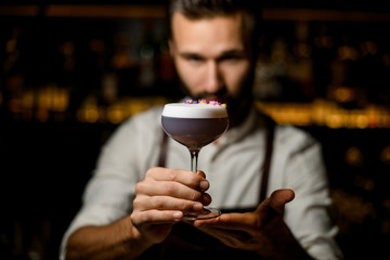 Male bartender serving a cocktail with white scum decorated with flower petals in the bar