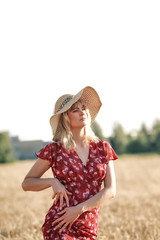 YOUNG AND BEAUTIFUL GIRL IN THE DRESS AND HAT ON THE WHEAT FIELD IN SUMMER