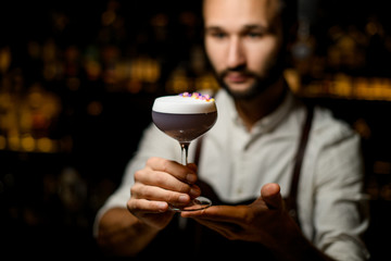 Professional male bartender serving a cocktail with white scum decorated with flower petals in the bar