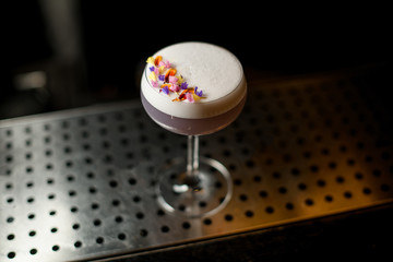 View from above glass of a delicious violet color cocktail decorated with different flower petals