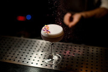 Bartender sprinkling on the cocktail with white scum decorated with flower petals a shredded flowers