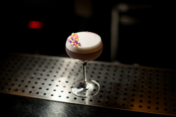Glass of a delicious violet color cocktail decorated with different flower petals