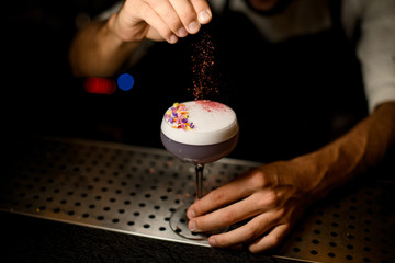 Male bartender sprinkling on the cocktail decorated with flower petals a shredded flowers