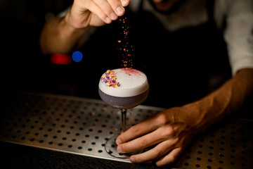 Professional bartender sprinkling on the cocktail decorated with flower petals a shredded flowers