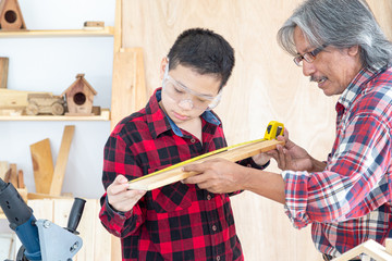 Asian boy and his father are using a tape measure to measure the length of the wood in carpentry shop. Family, carpentry, woodwork and people concept.