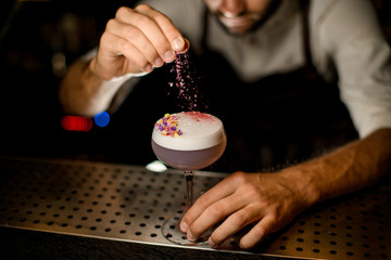 Bartender sprinkling on the cocktail decorated with petals a shredded flowers