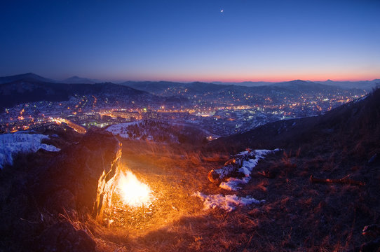 Night fire on the mountain on the background of the town village under a sunset sky