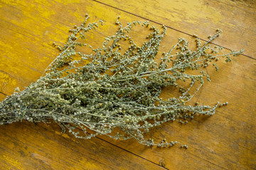 Dry bouquet of wormwood plants on a background of old yellow boards. View from above.