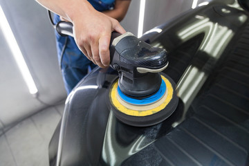 Obraz premium The polisher polishes the body of the vehicle with special wax to protect the car from minor scratches and damage, using a polishing eccentric machine to cover black hood after washing. Auto service