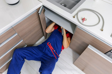 plumber working under domestic kitchen sink, repairing water pipes