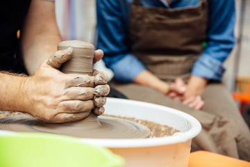 Senior woman spinning clay on a wheel with teacher at pottery class