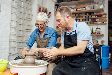 Senior woman spinning clay on a wheel with teacher at pottery class