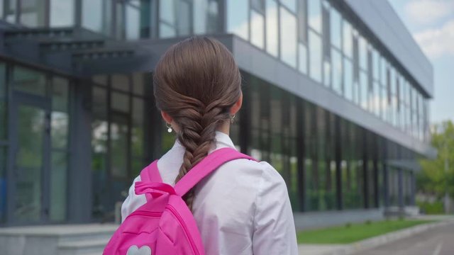back view of schoolgirl with backpack walking at schoolyard