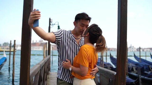Asian couple in love take a selfie in Venice, in front of the gondolas and they kiss
