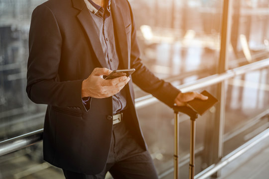 Businessman Using Mobile Phone At The Airport. Holding Passport With Luggage.Travel And Business Airport Concept.