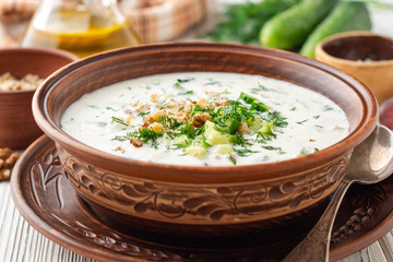 Traditional bulgarian cold summer soup tarator with yogurt, dill, cucumber and walnuts in ceramic bowl on wooden table. Selective focus.