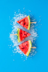 Cut watermelon on ice with fruit popsicle on blue background top view