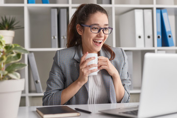 Excited employee with mug using laptop