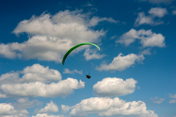 Alone paraglider flying in the blue sky against the background of clouds. Paragliding in the sky on a sunny day.