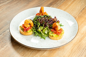 Fresh bruschetta with shrimp and salad on a white plate on a wooden background. Italian cuisine. Food photo background for menu or recipe. Seafood. appetizer before lunch