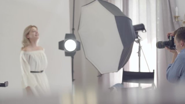 Backstage of the photo shoot. Professional male photographer dancing with a model in white dress before taking photos in the studio on white background. Photography, profession, photo session.