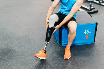 Disabled athlete assembling his leg prosthesis in the gym. Paralympic Sport Concept.