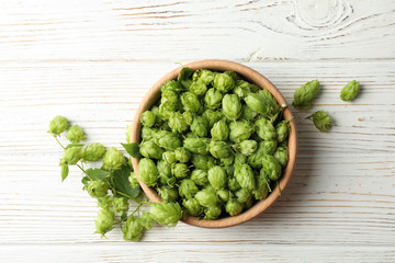 Wooden bowl with hop on white wood background, space for text