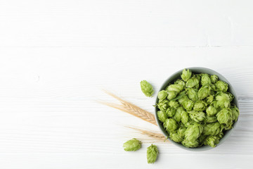 Bowl with hop and spikelets on white wooden background, space for text