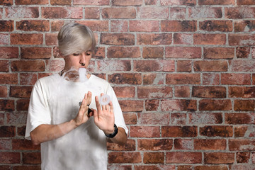 Vaper Smoke outdoor electronic cigarette near the brick wall. Young man smoking big cloud of steam