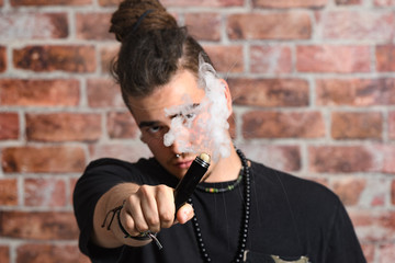Vaper Smoke outdoor electronic cigarette near the brick wall. Young man smoking big cloud of steam