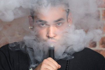 Vaper Smoke outdoor electronic cigarette near the brick wall. Young man smoking big cloud of steam